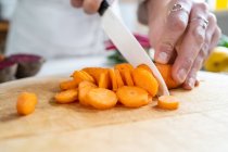 Ernte bis zur Unkenntlichkeit Weibchen schneiden rohe Karotte mit Messer bei der Zubereitung von vegetarischem Essen im Haus — Stockfoto