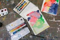 From above of watercolor paint palettes and abstract pictures arranged on table in creative studio — Stock Photo