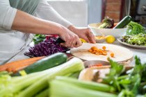 Ernte bis zur Unkenntlichkeit Weibchen schneiden rohe Karotte mit Messer bei der Zubereitung von vegetarischem Essen im Haus — Stockfoto