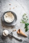 Dall'alto del cono di cialde vicino a misurini di gelato al latte di meringa e foglie di menta fresca sul tavolo di marmo — Foto stock