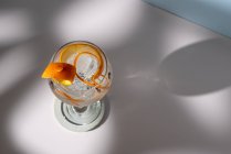 Top view of transparent glass of highball cocktail decorated with citrus fruit zest and clove against shadows in sunlight — Stock Photo