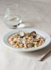Аппетитные традиционные испанские тушеные белые ткани фасоль с моллюсками в тарелке со свежими листьями петрушки на скатерти — стоковое фото