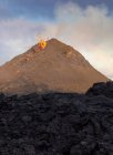 Vista lateral de las chispas de magma fuera del agujero del volcán y correr como ríos de lava sobre el suelo en Islandia - foto de stock