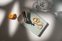 De cima de vidro perto de jigger metálico com raspas de frutas cítricas e condimentos secos na mesa com sombras — Fotografia de Stock