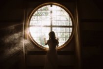 Back view of unrecognizable gentle female touching fence on round shaped window in house in sunlight — Stock Photo