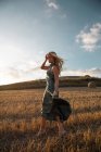Peaceful female in elegant dress standing on dry field in rural area and closed eyes — Stock Photo