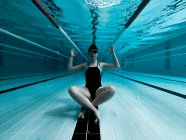 Женщина сидит под водой в позе йоги и смотрит в камеру — стоковое фото