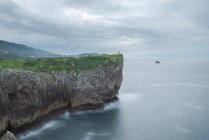 Silhouette de la personne debout sur le bord de la falaise rocheuse près de la mer sur la côte de Ribadesella par temps nuageux dans les Asturies — Photo de stock