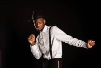 Giovane modello maschile etnico maschile maschile in cappello e pantaloni in piedi ballando su sfondo nero — Foto stock