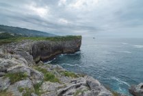 Breathtaking view of rough rocky cliff near calm sea on Ribadesella coast under gray sky in Asturias — Stock Photo