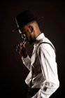 Side view of masculine African American male in white shirt and hat exhaling vapor while smoking e cigarette — Stock Photo