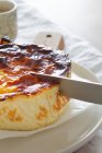 Zugeschnittene unkenntliche Person schneidet köstlichen gebackenen Käsekuchen mit Messer auf einem Teller serviert — Stockfoto