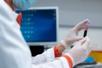 Неузнаваемая женщина-медик в маске и перчатках держит трубку с образцом крови в современной лаборатории в клинике — стоковое фото