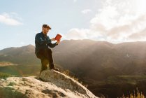 Чоловік-дослідник з планшетом, що стоїть на скелі і насолоджується вражаючим видом на гори в сонячний день — стокове фото
