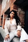 Confident plus size female in trendy coat sitting on stone border near old brick building and looking at camera — Stock Photo