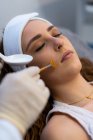 Анонимный культивист-косметолог наносит кислотный пилинг на лицо клиентки во время посещения клиники красоты — стоковое фото
