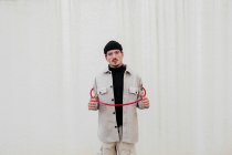 Fiducioso maschio in abiti alla moda in piedi con cerchio ginnico rosso contro il muro grigio di costruzione in città e guardando la fotocamera — Foto stock