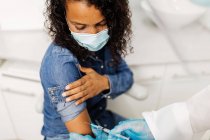 Unbekannter männlicher Facharzt in Schutzuniform und Latexhandschuhen impft afroamerikanische Patientin in Klinik während Coronavirus-Ausbruch — Stockfoto