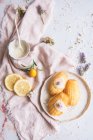 Вид сверху на вкусные мадлен на тарелке между свежими ломтиками лимона и цветущими веточками лаванды на мятой ткани — стоковое фото