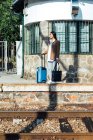 Азиатка-путешественница с чемоданом, стоящая на платформе железнодорожного вокзала в ожидании поезда — стоковое фото