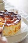 Cultivado irreconocible persona rebanando delicioso pastel de queso al horno con cuchillo servido en un plato - foto de stock
