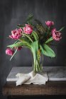 Fleurs roses fleuries avec des pétales doux et des feuilles vertes dans un vase sur fond gris — Photo de stock