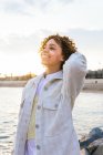Angle élevé de joyeuse femme afro-américaine debout avec les bras tendus sur les rochers sur le bord de la mer et jouissant de la liberté au coucher du soleil regardant loin — Photo de stock