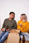 Fröhliches multiethnisches Paar sitzt zu Hause auf dem Fußboden, isst leckere Pizza und trinkt zusammen Bier — Stockfoto