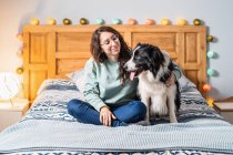 Junge Frau mit Brille sitzt mit Border-Collie-Hund im Bett — Stockfoto