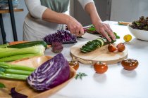 Кукурудза невизначена жінка, що ріже кабачки з ножем, готуючи обід за кухонним столом в будинку — стокове фото