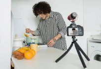 Jovem de camisa listrada falando contra câmera fotográfica em tripé durante processo de cozimento na cozinha — Fotografia de Stock