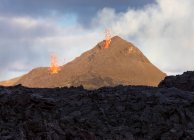 Vista lateral de faíscas de magma para fora do buraco do vulcão e correr como rios de lava sobre o chão na Islândia — Fotografia de Stock