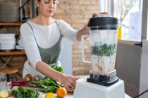Crop feminino mistura de folhas de acelga com leite vegetariano em aparelho de cozinha enquanto prepara bebida saudável em casa — Fotografia de Stock