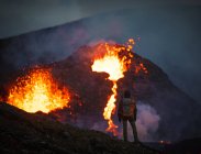 Man explorer observing the magma sparks out of the volcano Fagradalsfjall in Iceland between clouds of smoke — Stock Photo