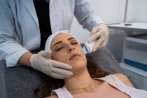 Crop unrecognizable cosmetologist doing ultrasonic face peeling for relaxed woman lying on medical table in modern beauty clinic — Stock Photo