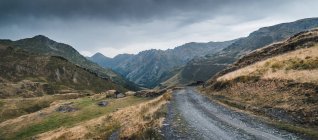 Malerische Landschaft der leeren Route mit trockenem und grünem Gras in bergigem Gelände des Aran-Tals in Spanien unter grauem wolkenverhangenem Himmel — Stockfoto