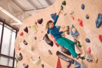 Female athlete climbing artificial wall during bouldering workout in professional gym — Stock Photo