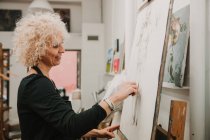 Artista donna che crea disegno di umano con matita mentre in piedi al cavalletto in studio — Foto stock