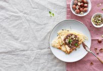 Vista dall'alto di deliziose crepes guarnite con cioccolato e noci servite sul piatto a colazione — Foto stock
