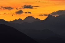 Breathtaking view of silhouettes of mountain peaks on background of bright orange sundown sky — Stock Photo