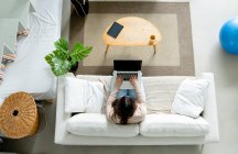 Hohe Winkel anonymer Frauen surfen im Internet auf tragbarem Computer mit schwarzem Bildschirm, während sie zu Hause auf dem Sofa liegen — Stockfoto