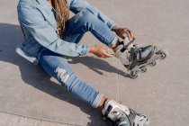 From above of African American female in denim outfit putting on rollerblades on sunny day in skate park — Stock Photo