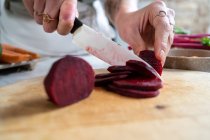Неузнаваемая женщина режет свежую свеклу ножом во время приготовления вегетарианского обеда на домашней кухне — стоковое фото