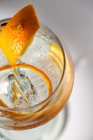 Vue de dessus du verre transparent de cocktail highball décoré de zeste d'agrumes et clou de girofle contre les ombres au soleil — Photo de stock