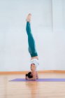 Side view of anonymous flexible female in sportswear standing on head with raised legs while practicing yoga in house — Stock Photo