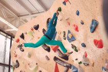 Vista posteriore a basso angolo di anonima parete artificiale di arrampicata atletica femminile durante l'allenamento di boulder in palestra professionale — Foto stock