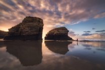 Silhueta de pessoa anônima em pé sobre molhado Como praia de Catedrais com rochas sob o céu do pôr-do-sol na Galiza — Fotografia de Stock