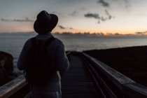 Mann mit Rucksack und Hut steht und blickt aufs Meer — Stockfoto