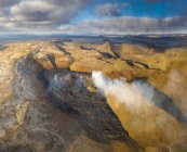 From above columns of smoke and magma sparks out of the volcano hole and run like rivers of lava over the ground in Iceland — Stock Photo