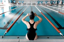 Nuotatore seduto sul bordo della piscina e mettere i suoi occhiali da nuoto — Foto stock